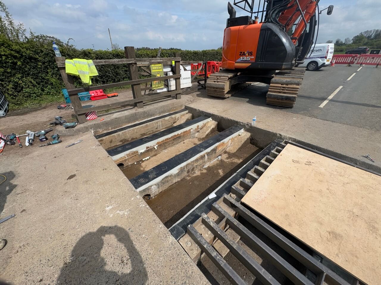 Lifting a cattle grid out with a tracked excavator during the B3134 refurbishment, sleeper walls exposed